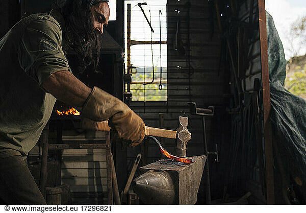 Blacksmith working a piece of red-hot steel with a sledgehammer.