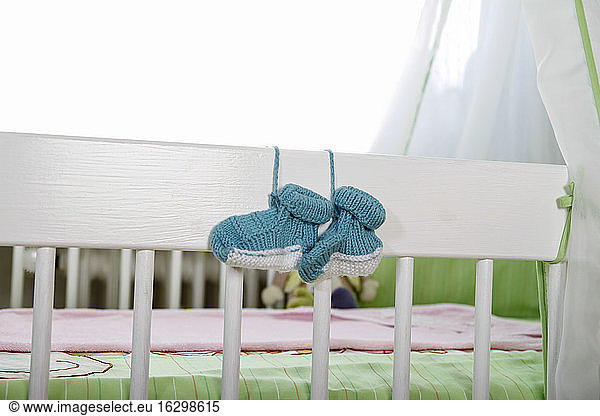Blaue Babyschuhe hängen am Kinderbett
