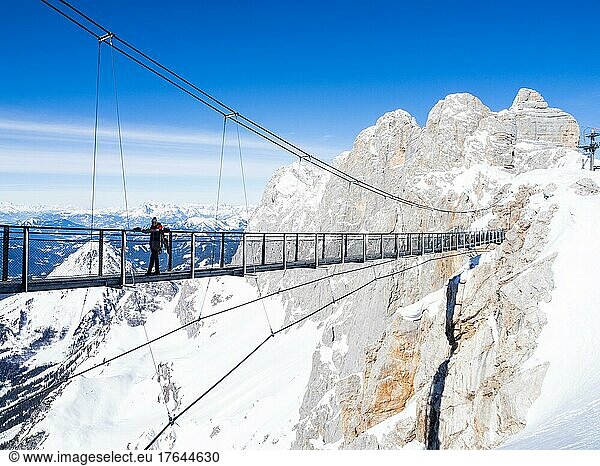 Blauer Himmel über alpiner Winterlandschaft  Touristin auf der Hängebrücke am Dachstein  Dachsteingletscher  Steiermark  Österreich