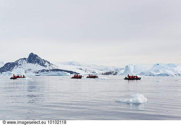 Blick auf Personengruppen in Gummibooten in der Nähe und Eisberg in der Antarktis.