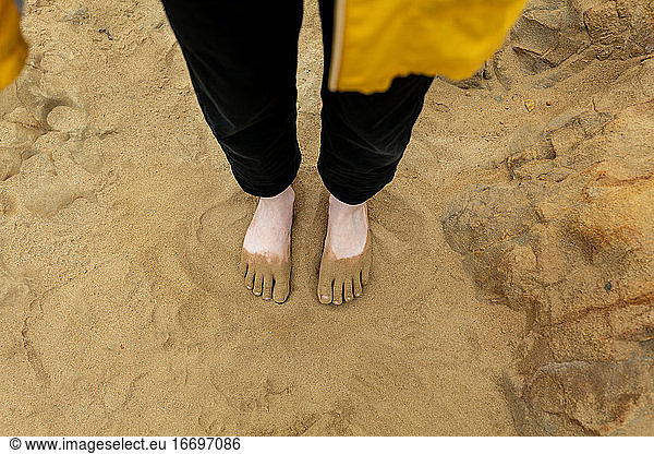 Blick nach unten auf junge Menschen Füße in Sand am Strand bedeckt