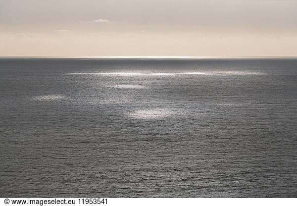 Blick vom Land über den Ozean bis zum Horizont. Sonnenlichtflecken auf der Wasseroberfläche.
