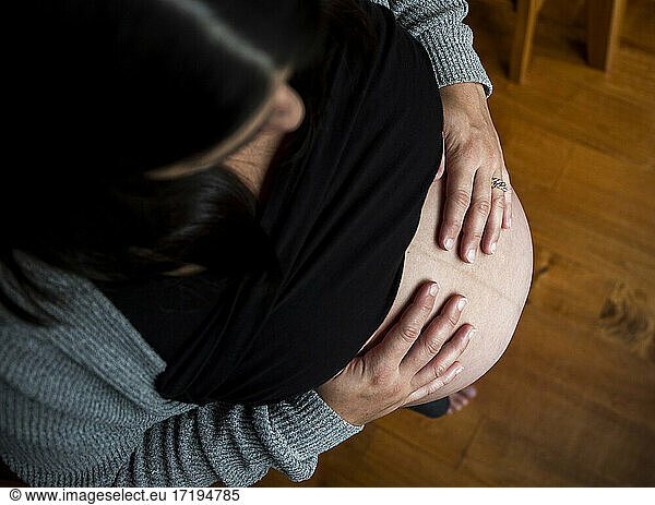Blick von oben auf eine schwangere Frau  die ihren Bauch zu Hause mit den Händen berührt