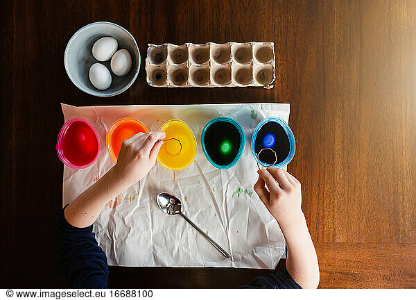 Blick von oben auf Kinderhände  die Ostereier auf einem Holztisch färben.