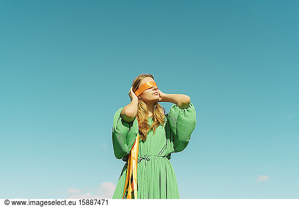 Blindfolded young woman wearing a green dress under blue sky