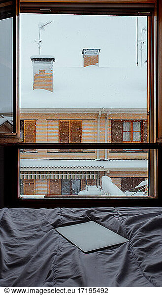 Blizzard against building seen from the bed with a laptop. Snowy day