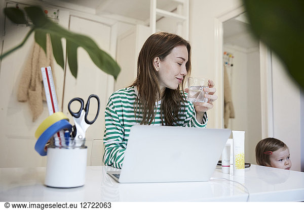 Blogger with laptop drinking water while looking at daughter