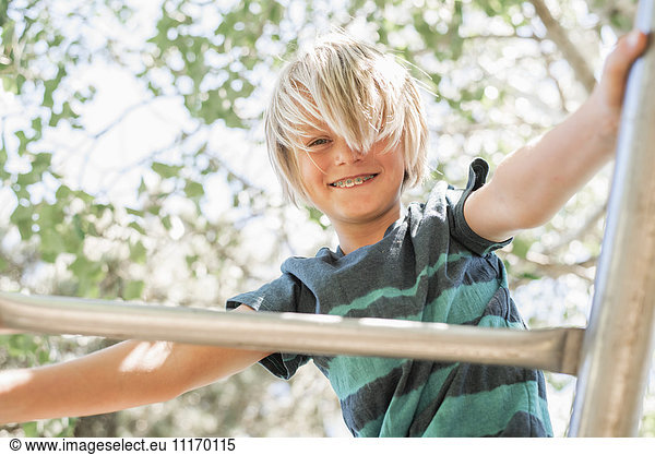 Blond boy on a climbing frame in a garden.