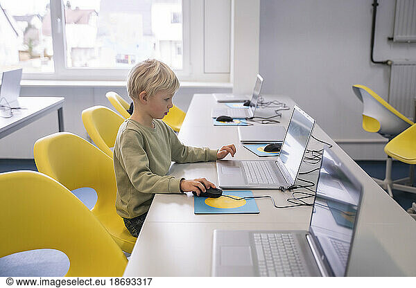 Blond boy using laptop sitting on chair at school