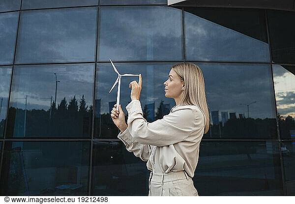 Blond businesswoman examining and touching wind turbine model