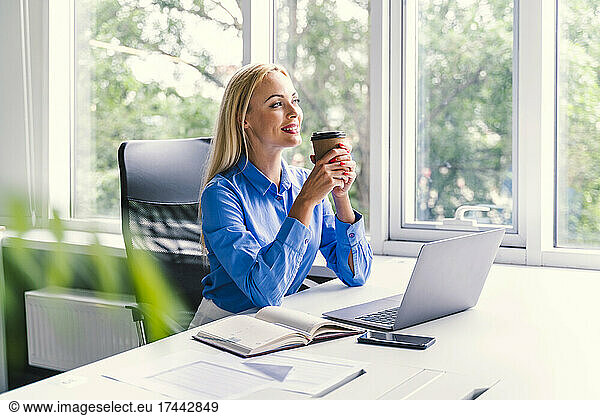 Blond businesswoman having coffee while sitting at desk in office