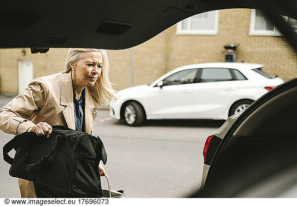 Blond businesswoman loading luggage in car trunk