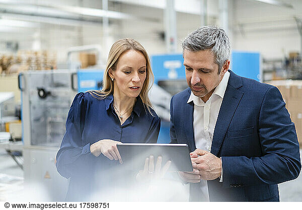Blond businesswoman sharing tablet PC with colleague in factory