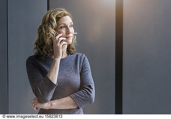 Blond businesswoman using smartphone and looking out of the window