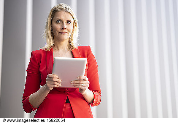Blond businesswoman wearing red suit and using digital tablet