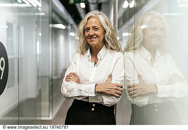 Blond businesswoman with arms crossed leaning on glass wall in office