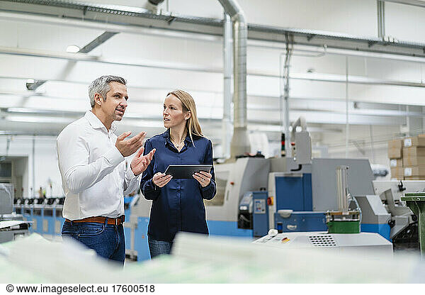 Blond businesswoman with tablet PC looking at colleague discussing in industry