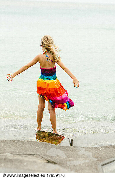 Blond caucasian girl in rainbow dress with wind on ocean