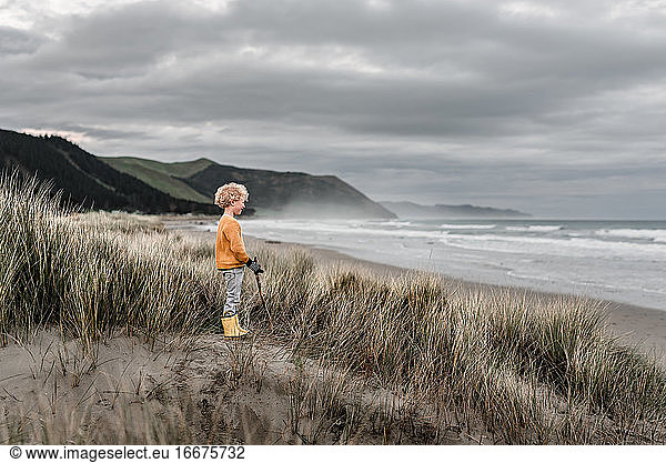 Blond curly haired boy watching ocean on cloudy day in New Zealand