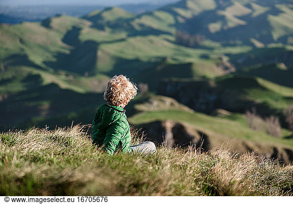Blond curly haired child looking at view of green hills