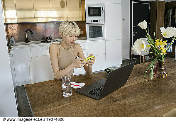 Blond freelancer using smart phone in kitchen