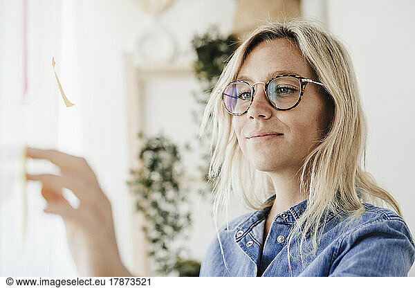 Blond freelancer with eyeglasses sticking adhesive note