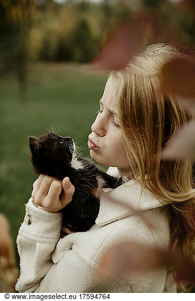 Blond girl carrying kitten and puckering in garden