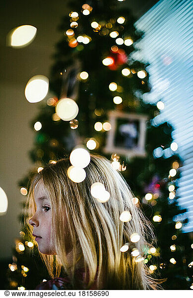 Blond girl child in front of Christmas tree with lights and ornaments