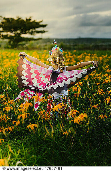 Blond girl child pretend play with butterfly wings in flower field