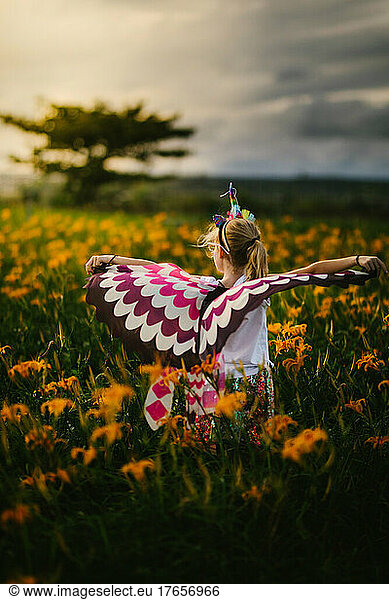 Blond girl child with butterfly wings in orange flower field playing