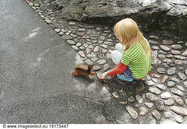 Blond girl feeding squirrel on street