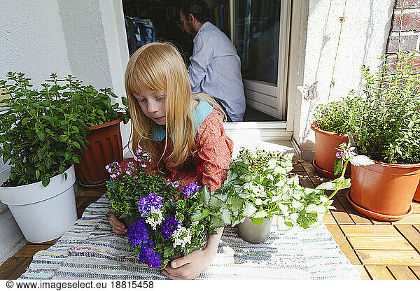 Blond girl holding plant sitting in balcony
