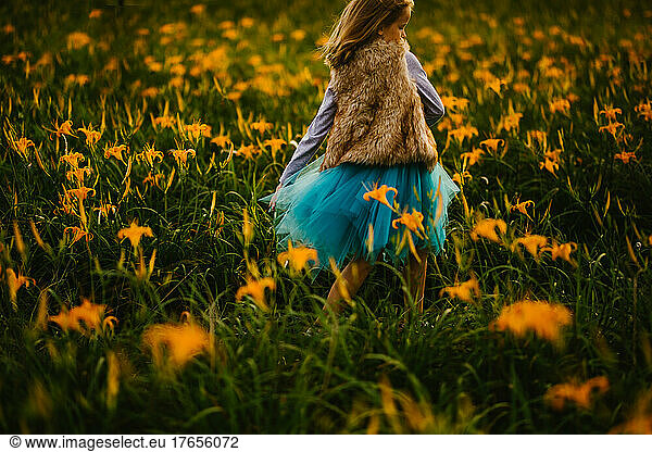 Blond girl in blue skirt twirls in orange lily flower field