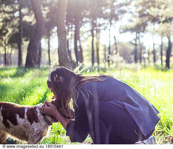 blond girl kissing on the head her dog in the forest