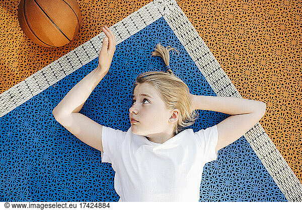 Blond girl looking at ball while lying down in sports court