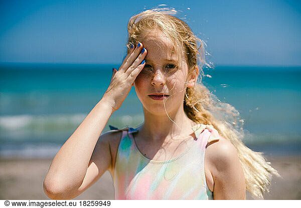 Blond girl rubs sunscreen into face on summer vacation sunny day
