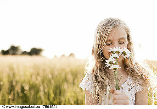 Blond girl smelling flowers in field