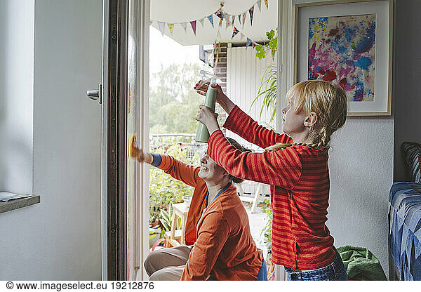Blond girl spraying water and elder sister cleaning door of balcony