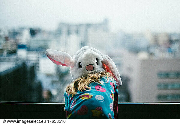 Blond girl wearing bunny hat looks over city scape