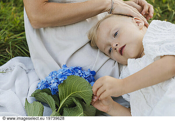 Blond girl with blue flowers lying on mother's lap