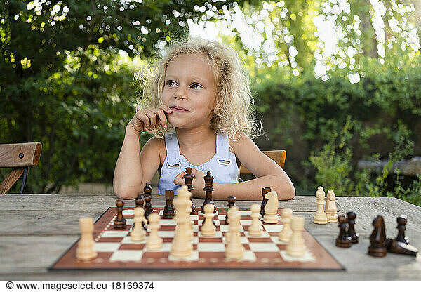 Blond girl with chessboard on table in garden