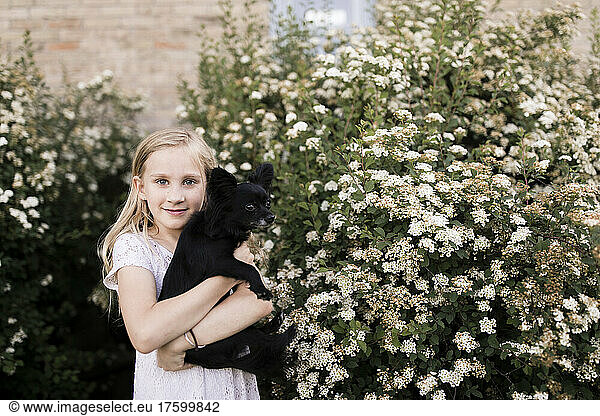 Blond girl with dog by white flowering plant