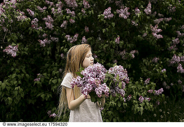 Blond girl with eyes closed holding lilac flowers in nature