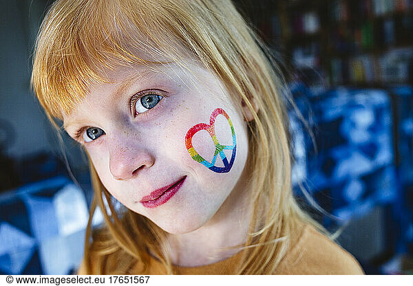 Blond girl with peace sticker on cheek at home
