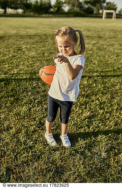 Blond girl with rugby ball gesturing at sports field