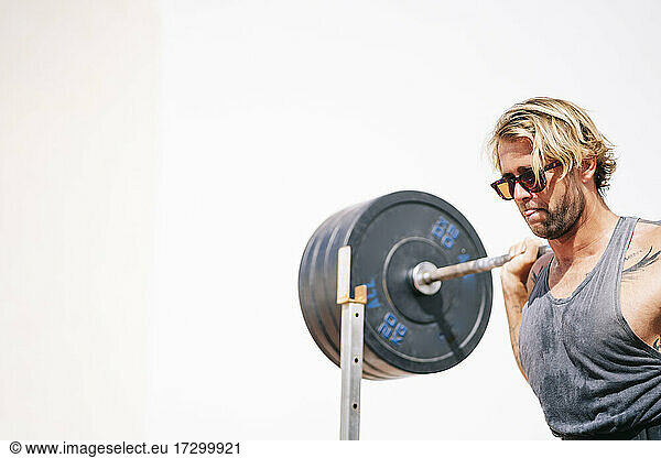 Blond haired man with suffering face holding dumbbells