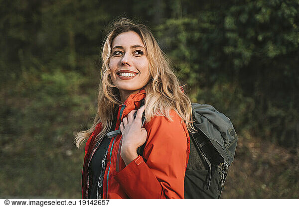 Blond happy woman with backpack in forest