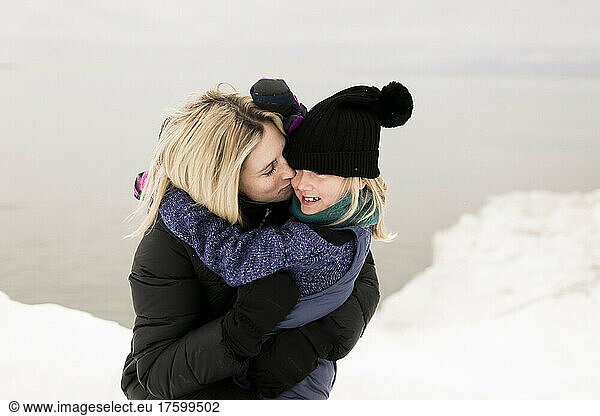 Blond mother kissing daughter in winter