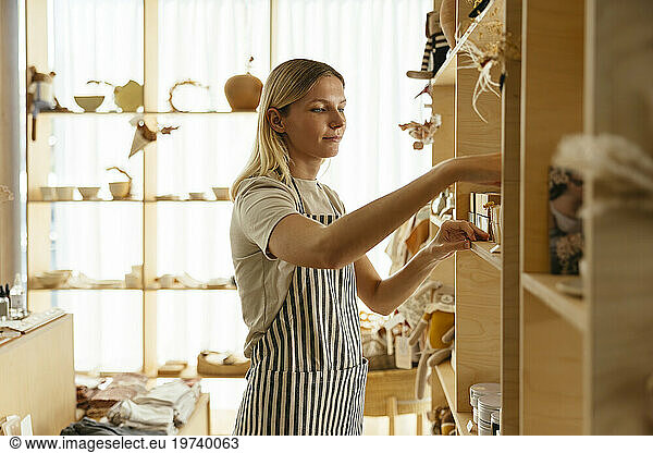 Blond owner arranging products on shelf at store