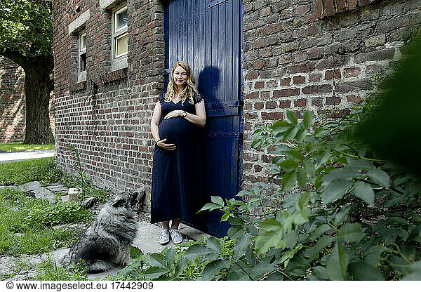 Blond pregnant woman with dog standing at doorway